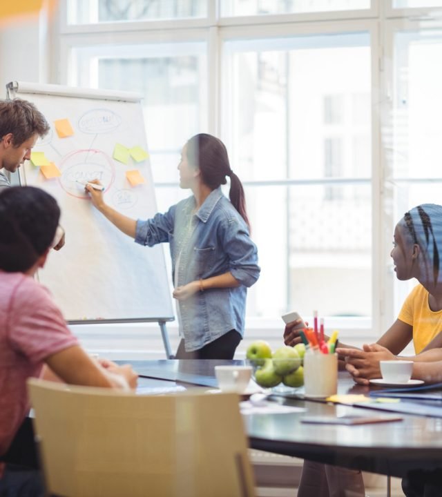Business executives discussing with their colleagues on whiteboard Business executives discussing with their colleagues on whiteboard during meeting at office